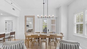 A dining area with a wooden table and chairs, a chandelier, and a large mirror. - Lazy Duck Retreat by Avantstay Blue Mountain Priv Beach Access Pool + Patio (Santa Rosa Beach)