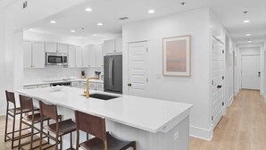 A modern kitchen with white cabinetry, a central island with bar stools, stainless steel appliances, and recessed ceiling lighting. - Lazy Duck Retreat by Avantstay Blue Mountain Priv Beach Access Pool + Patio (Santa Rosa Beach)