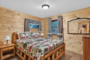 A wooden cabin bedroom with a bed, bedside tables, a mirror, and curtains.