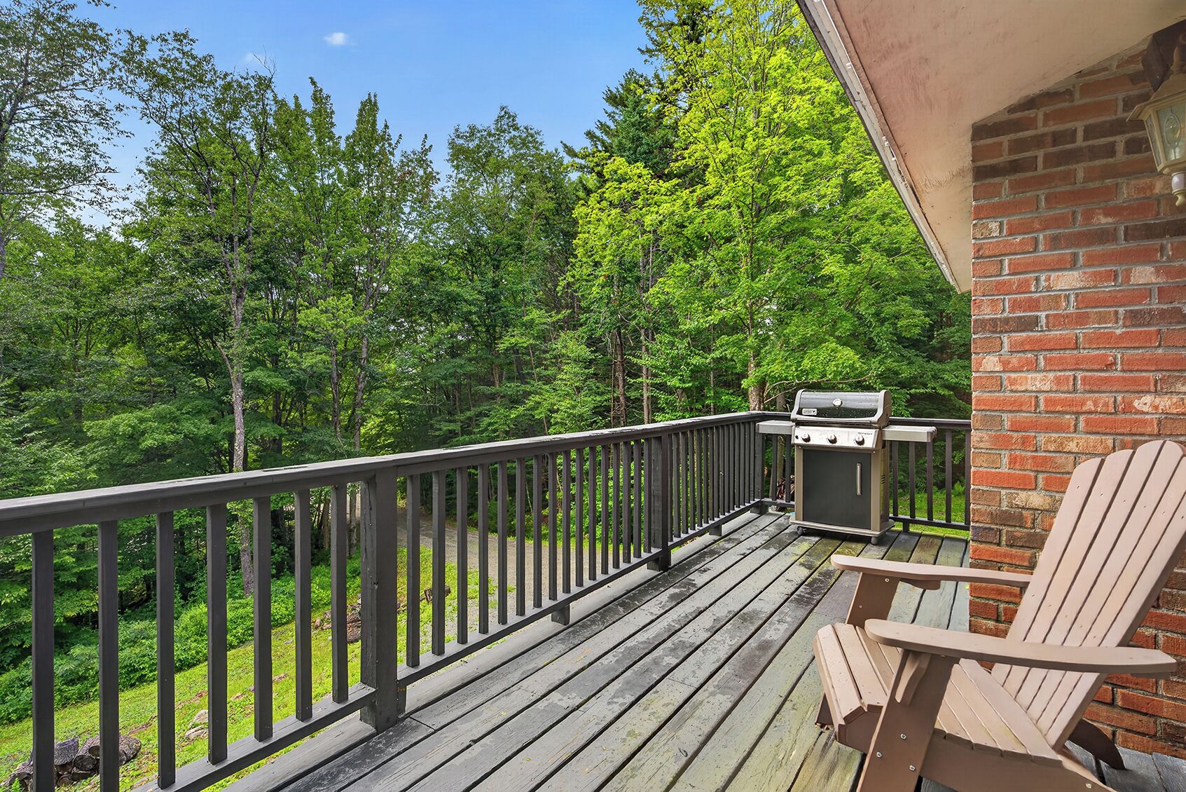 A deck with a grill and a chair, surrounded by trees.
