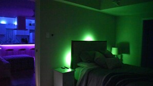 Een kamer in gedempt licht met een bed, een nachtkastje en een groen verlichte muur.