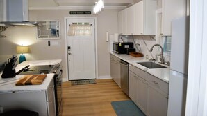 Een kleine keuken met witte kastjes, een magnetron, een spoelbak en een houten snijplank op het aanrecht.