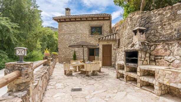 Un bâtiment en pierre doté d’un patio comprenant une table et des chaises, un barbecue et une lanterne.