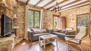 Un salon chaleureux avec des murs en pierre, une cheminée, un canapé, un fauteuil et un téléviseur.