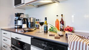 Et moderne køkken med indbygget ovn, mikroovn og kaffemaskine. Der er flere flasker og en skål på bordet.