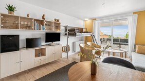 En kompakt opholdsstue med TV, tekøkken og en balkon med udsigt.