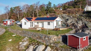 A white house with a red roof, a stone retaining wall, and a red shed. - Cozy home in Kållekärr with WiFi (Kållekärr)
