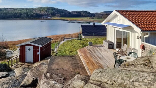 A lakeside property with a wooden deck, a small shed, and a house with a red roof. - Cozy home in Kållekärr with WiFi (Kållekärr)