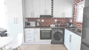 Una cocina compacta con armarios blancos, microondas, estufa, lavadora y refrigerador.