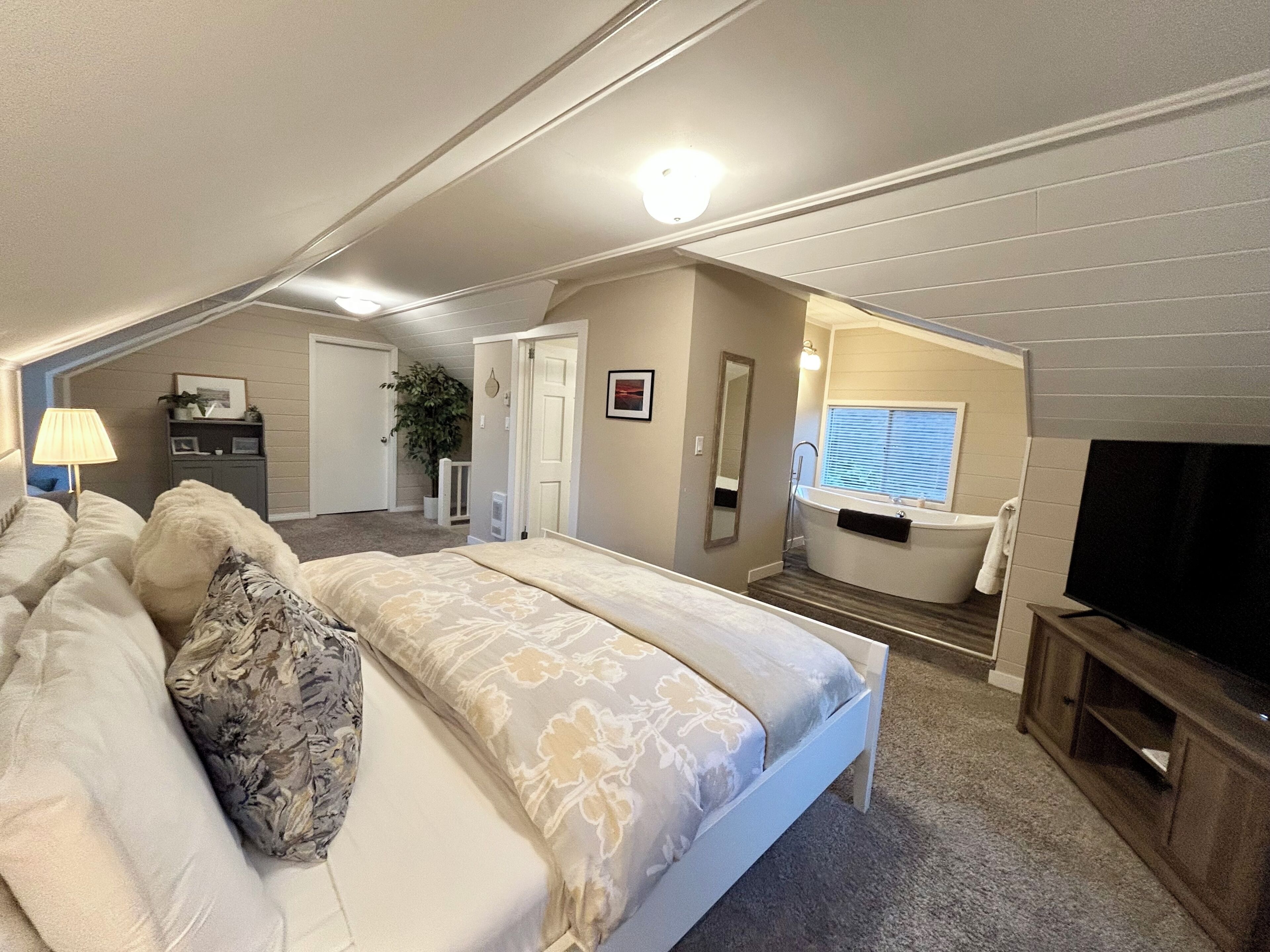 Een slaapkamer met een bed, een televisie, een badkamer met bad en een gang die naar een andere kamer leidt.
