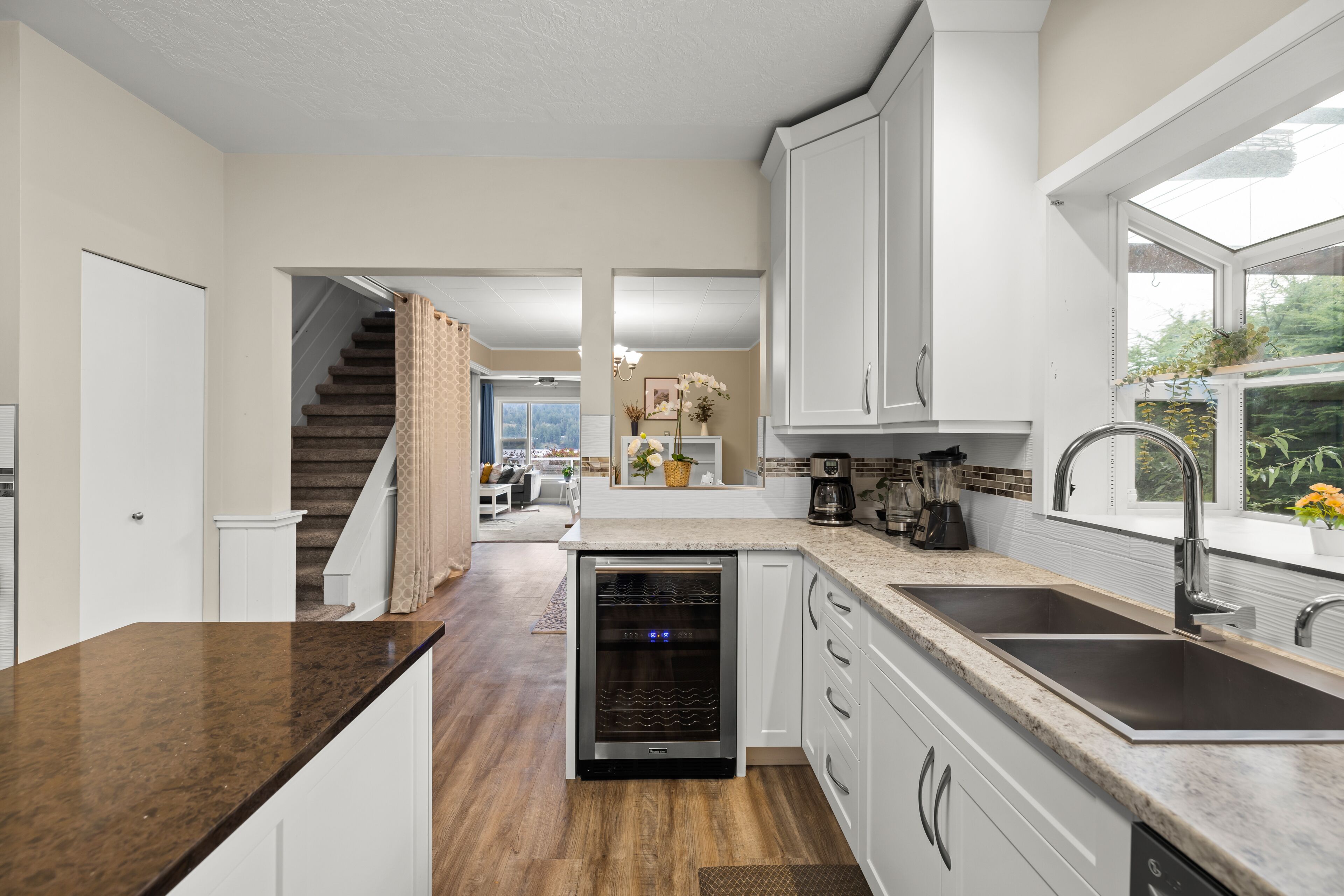 A kitchen with a dishwasher, double sink, and a window with plants.