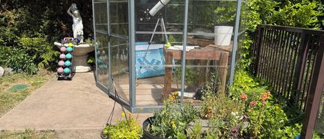 A greenhouse with a clear roof, a thermometer, and a table with a lamp.
