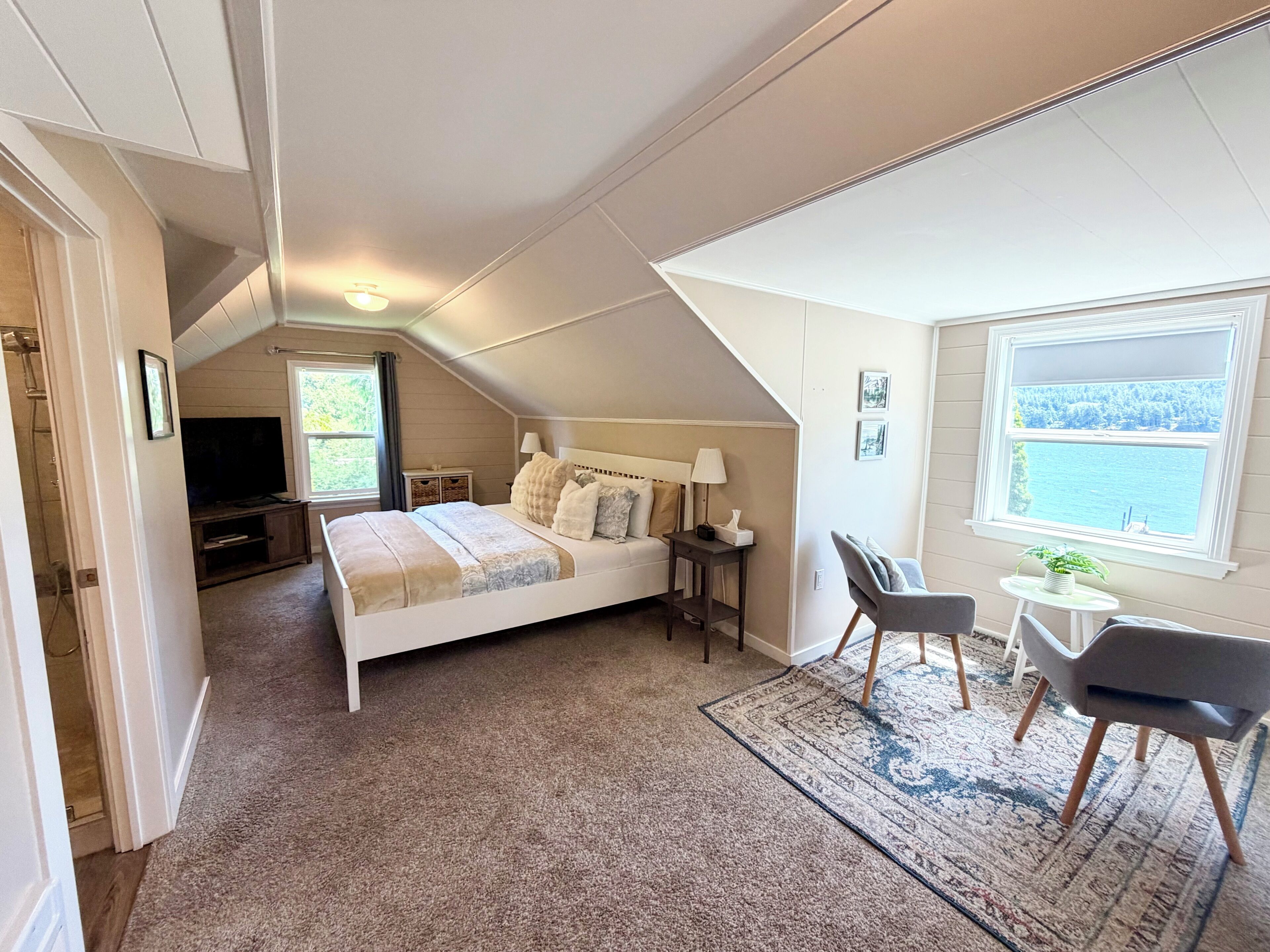 A bedroom with a bed, bedside tables, a TV, a window with a view, and a small table with chairs.