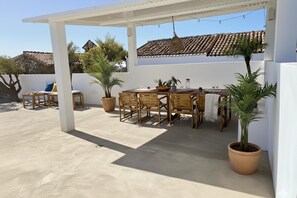 An outdoor patio with a table and chairs, potted plants, and a white wall.