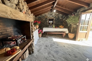 A rustic stone-walled room with a stone fireplace, a wooden table set with a white tablecloth, and a potted plant.