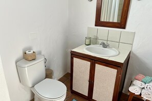A bathroom with a toilet, sink, mirror, and a small towel rack with folded towels.