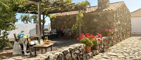 A stone building with a pergola, outdoor seating, and potted flowers.