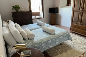 A bedroom with a bed, pillows, a bedside lamp, a dresser, a television, and a window.