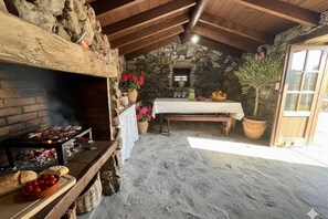 Una habitación rústica con paredes de piedra, una chimenea de piedra, una mesa de madera cubierta con un mantel blanco y una planta en maceta.