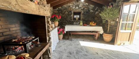 A rustic stone-walled room with a stone fireplace, a wooden table set with a white tablecloth, and a potted plant.