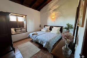 A bedroom with a bed, a window, a nightstand, a vase with flowers, and a painting on the wall.