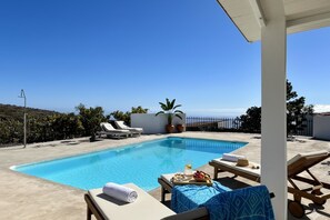 A pool area with lounge chairs, a table with drinks, and a view of the sea.