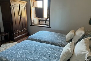 A bedroom with two beds, a window seat, a wardrobe, and a small table. - Stunning El Poleo Cottage at El Estanco Viejo: Historic Comfort With B (Adeje)