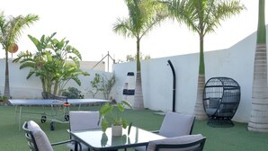 Un patio con mesa y sillas, rodeado de césped artificial y palmeras.