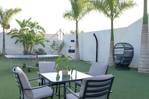 A patio with a table and chairs, surrounded by artificial grass and palm trees.