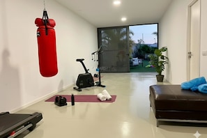 Un gimnasio con equipo de ejercicio, saco de boxeo, cinta de correr y banco.