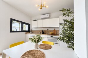 A modern kitchen with white cabinets, a black-framed window, and a dining table with yellow chairs. - Live the experience of a stylish Loft! (Aldea Blanca)