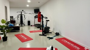 Un gimnasio con equipo de ejercicio, cinta de correr y colchonetas rojas con la marca 'CANARURAL'.