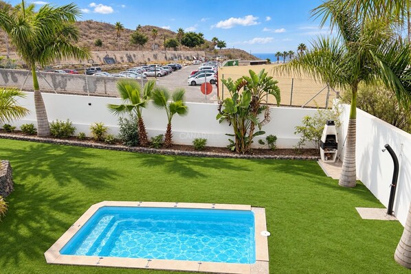 A swimming pool with a view of a parking lot and hills in the background.