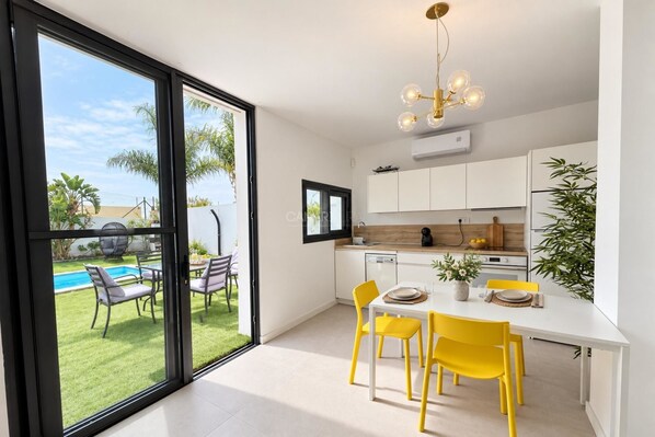 A modern kitchen with a dining area, large windows, and a view of a pool and greenery.