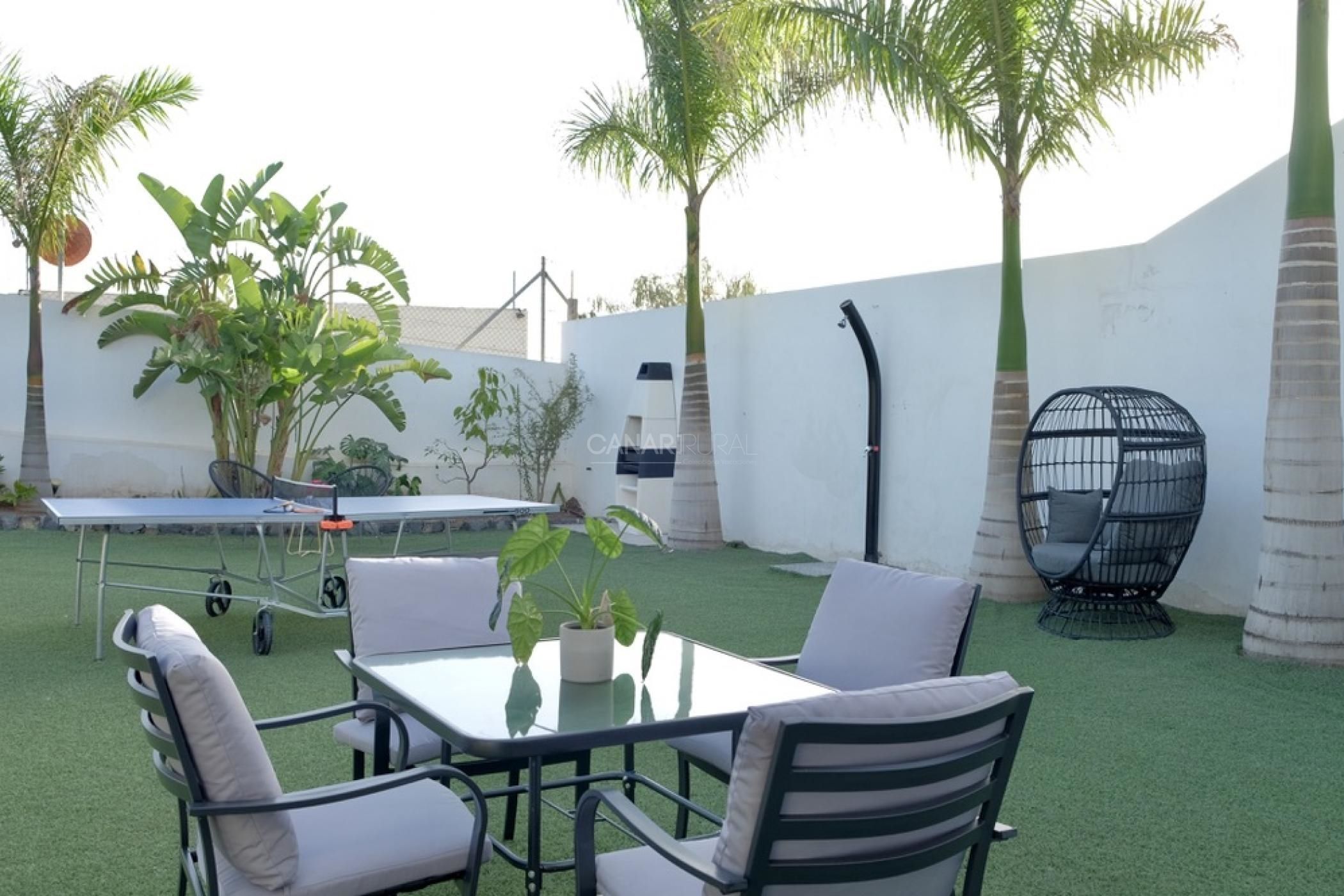 Un patio con mesa y sillas, rodeado de césped artificial y palmeras.