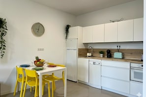 Una cocina moderna con armarios blancos, un refrigerador blanco, encimera de madera y comedor con mesa blanca y sillas amarillas.