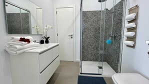 Un baño moderno con cabina de ducha de vidrio, tocador blanco y un inodoro.