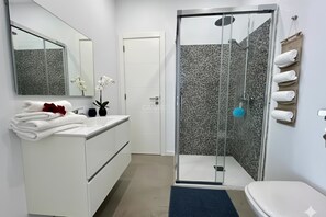 Moderni kylpyhuone, jossa on lasinen suihkuseinä, valkoinen allaskaappi ja wc-istuin.
