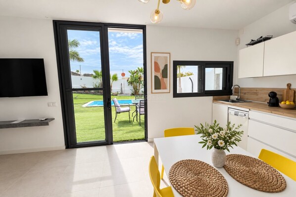 A modern kitchen with a dining area, a pool view, and a flat-screen TV mounted on the wall.
