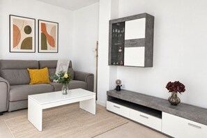 A modern living room with a grey sofa, a white coffee table, and a grey cabinet with a glass shelf.