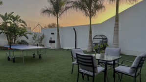 Un patio con césped artificial, una mesa de ping pong y una mesa con sillas.