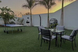 A patio with artificial grass, a ping pong table, and a table with chairs.