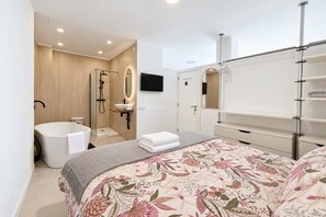 A modern bedroom with a large bed, a built-in bathtub, a vanity with a mirror, and a television. - Live the experience of a stylish Loft! (Aldea Blanca)