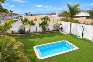 A swimming pool surrounded by artificial grass, palm trees, and a white fence.