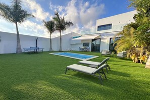 A modern house with a swimming pool, a tennis table, and a patio with lounge chairs.