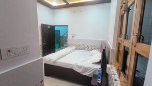 A bedroom with a bed, a water bottle on a nightstand, a ceiling fan, and a window with wooden frames. - Rudra Inn (Faizabad)