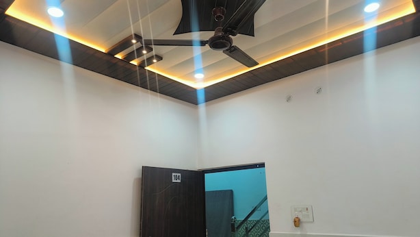 A modern hotel room with a ceiling fan, recessed lighting, and a door marked with the number 104. - Rudra Inn (Faizabad)