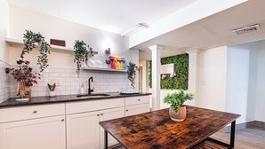 A modern kitchen with white cabinets, a black countertop, and a wooden table. - Adams Village 6-Bed Apt: City Perks, Suburban Vibe (Boston)