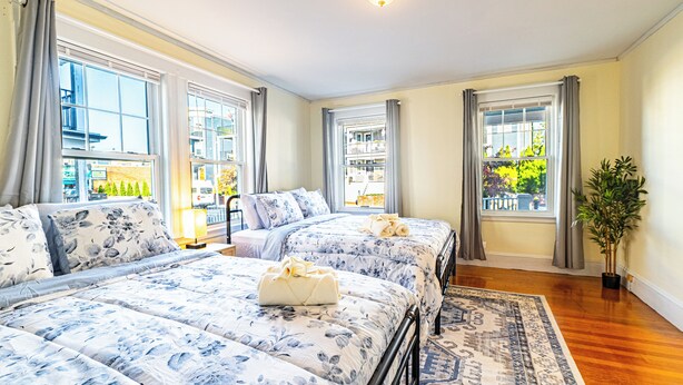 A hotel room with three beds, large windows, and a view of the city. - Adams Village 6-Bed Apt: City Perks, Suburban Vibe (Boston)