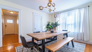 A dining area with a wooden table, black chairs, a bench, and a chandelier. - Adams Village 6-Bed Apt: City Perks, Suburban Vibe (Boston)